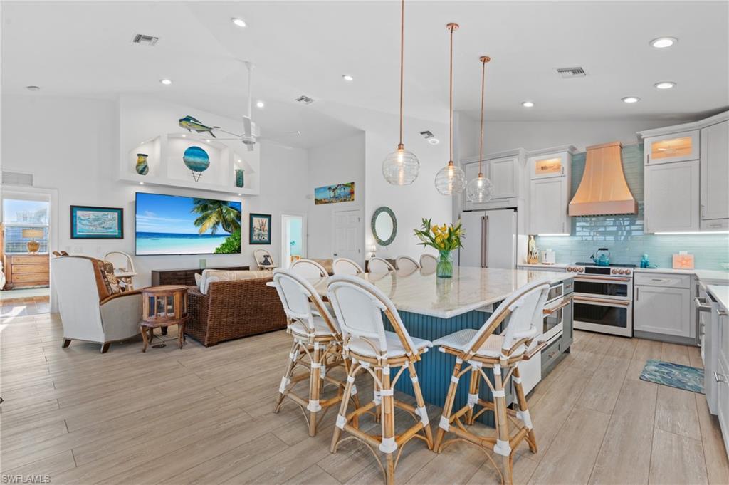 256 Curlew Street Fort Myers Beach, FL 33931 - Photo 12 of 43 Kitchen featuring premium range hood, white cabinetry, high quality appliances, decorative light fixtures, and vaulted ceiling. virtually enhanced photo
