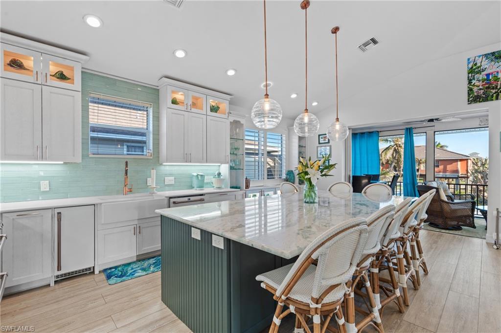 256 Curlew Street Fort Myers Beach, FL 33931 - Photo 13 of 43 Kitchen with sink, a center island with sink, white cabinets, pendant lighting, and backsplash. virtually enhanced photo