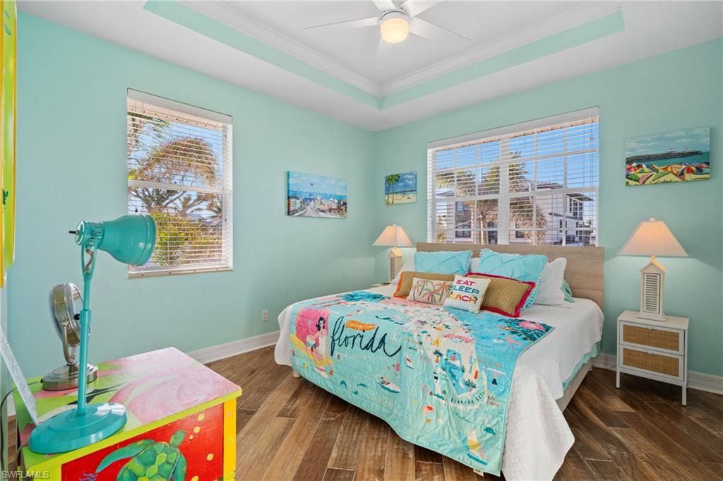 256 Curlew Street Fort Myers Beach, FL 33931 - Photo 23 of 43 Bedroom featuring dark wood-type flooring, ceiling fan, a tray ceiling, and multiple windows. virtually enhanced photo