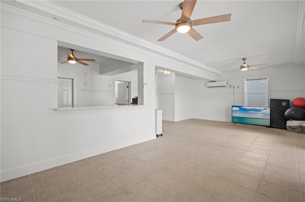 256 Curlew Street Fort Myers Beach, FL 33931 - Photo 30 of 43 Unfurnished living room featuring ornamental molding, a wall unit AC, and light tile patterned floors. virtually enhanced photo