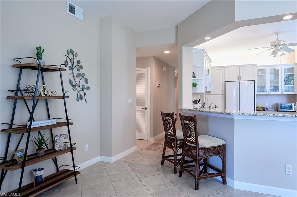 2371 Ravenna Boulevard, Unit 101 Naples, FL 34109 - Photo 6 of 44 Kitchen with white refrigerator, a breakfast bar area, white cabinets, light tile patterned floors, and light stone countertops