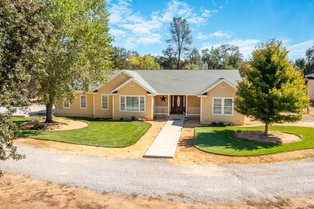 a view of a white house with a yard plants and large tree