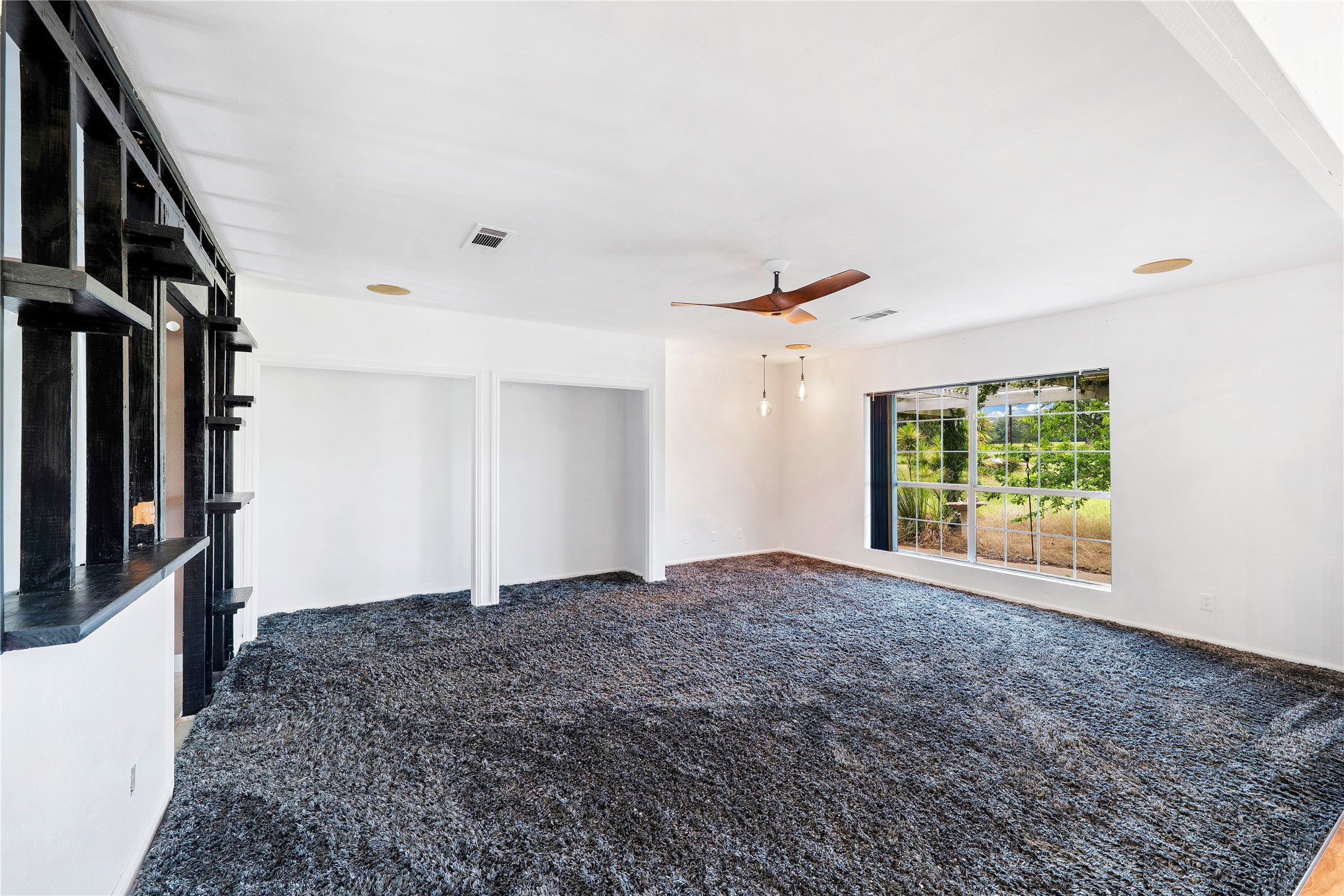 358 Easley Road Smithville, TX 78957 - Photo 21 of 36 Living area with warm lighting, built-in shelving, and a large window overlooking lush greenery.