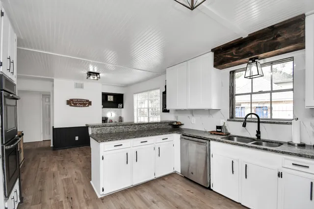 a kitchen with a sink dishwasher a stove and white cabinets with wooden floor