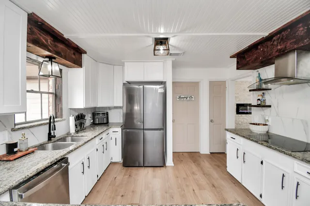 a kitchen with granite countertop a refrigerator a sink dishwasher a stove and white cabinets with wooden floor