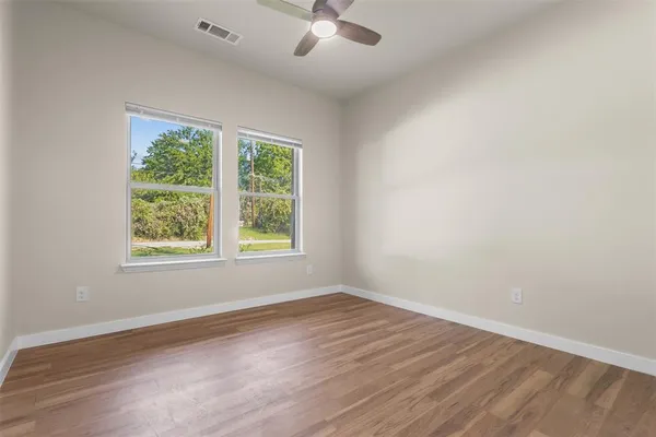 an empty room with wooden floor chandelier fan and windows