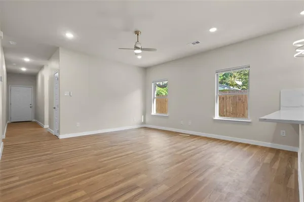 a view of an empty room and kitchen with wooden floor