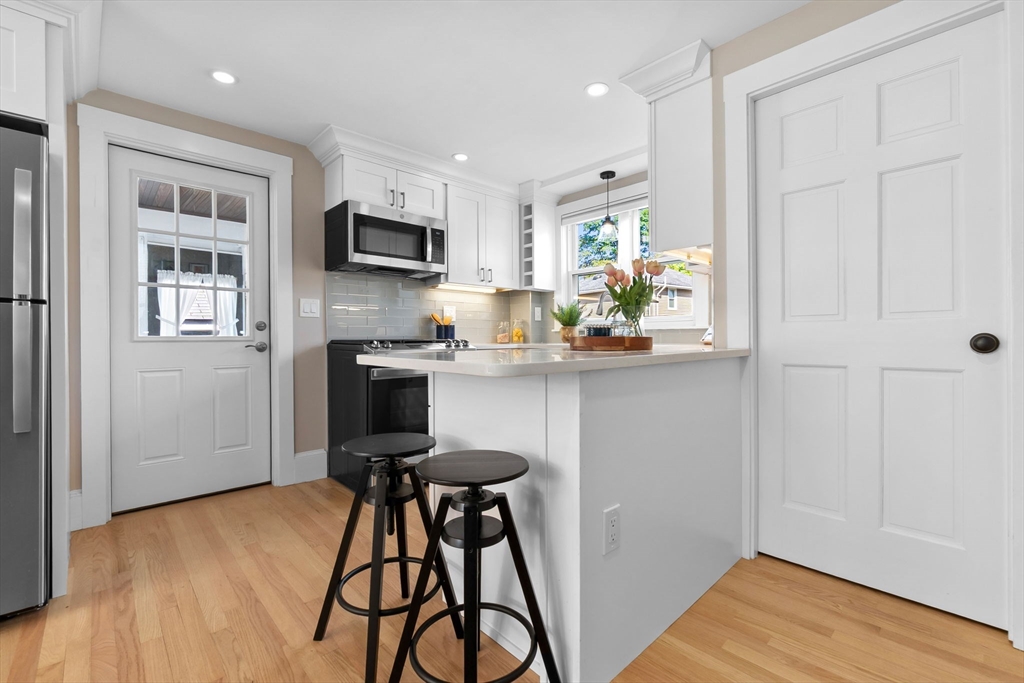 17 Coolidge Street Stoneham, MA 02180 - Photo 8 of 37 a kitchen with stainless steel appliances a stove a refrigerator a sink a dining table and chairs with wooden floor