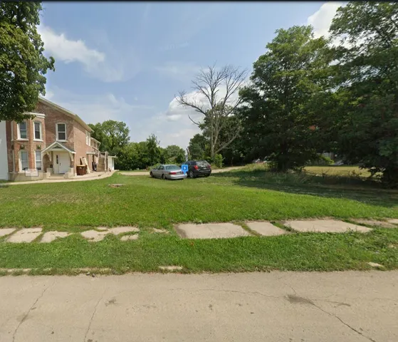 a view of a white house with a big yard and potted plants and large trees