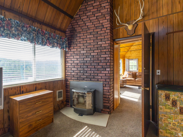 4770 Pine Crest Road Evanston, UT 82930 - Photo 20 of 24 Brick fireplace with wood-burning insert, wood-paneled walls and ceiling, and carpeted flooring