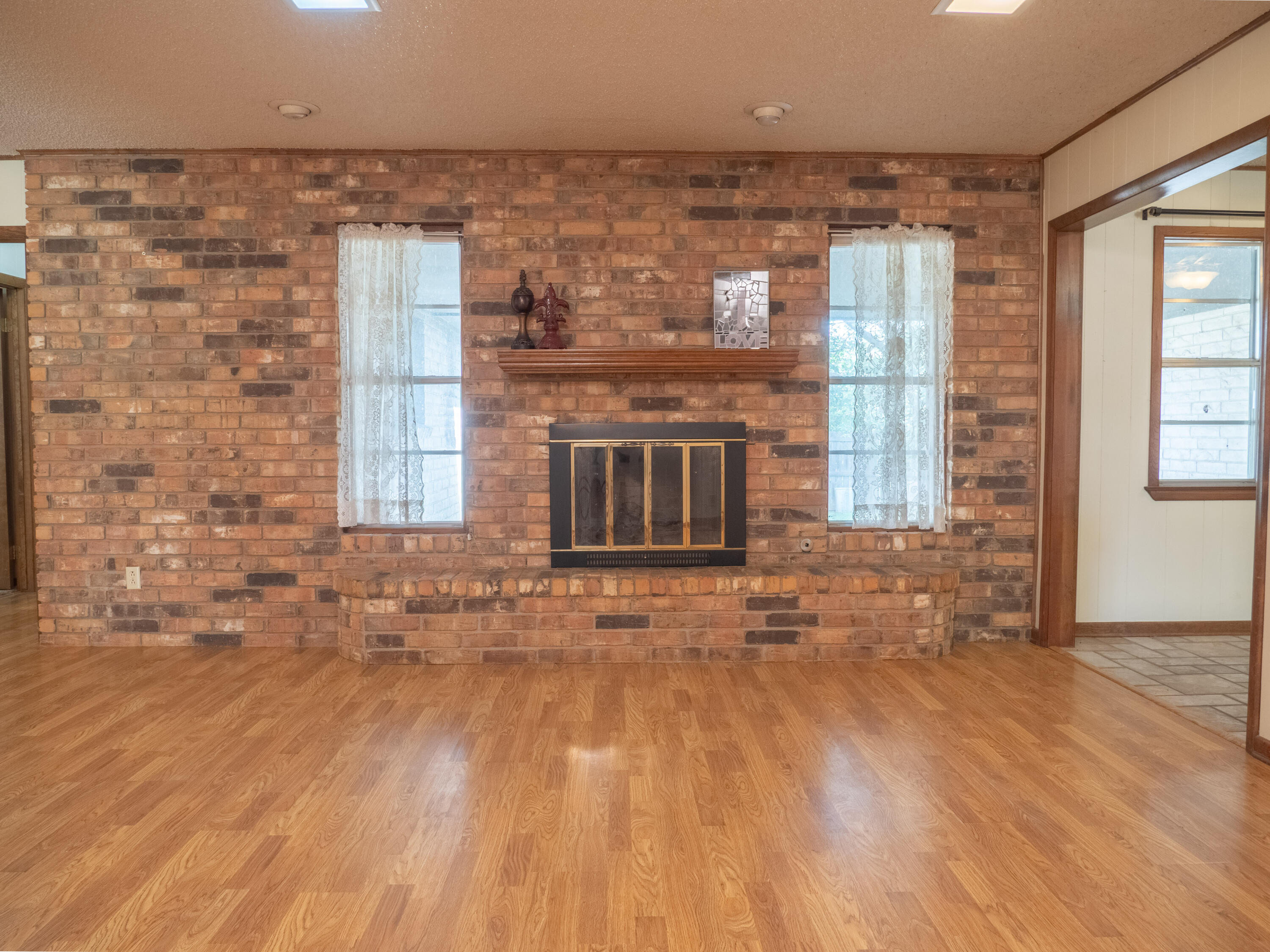 303 Comanche Trail Tulia, TX 79088 - Photo 7 of 37 an empty room with wooden floor and a fireplace