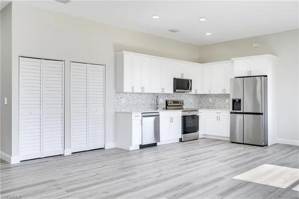 a kitchen with a refrigerator a stove top oven a sink and white walls with wooden floor