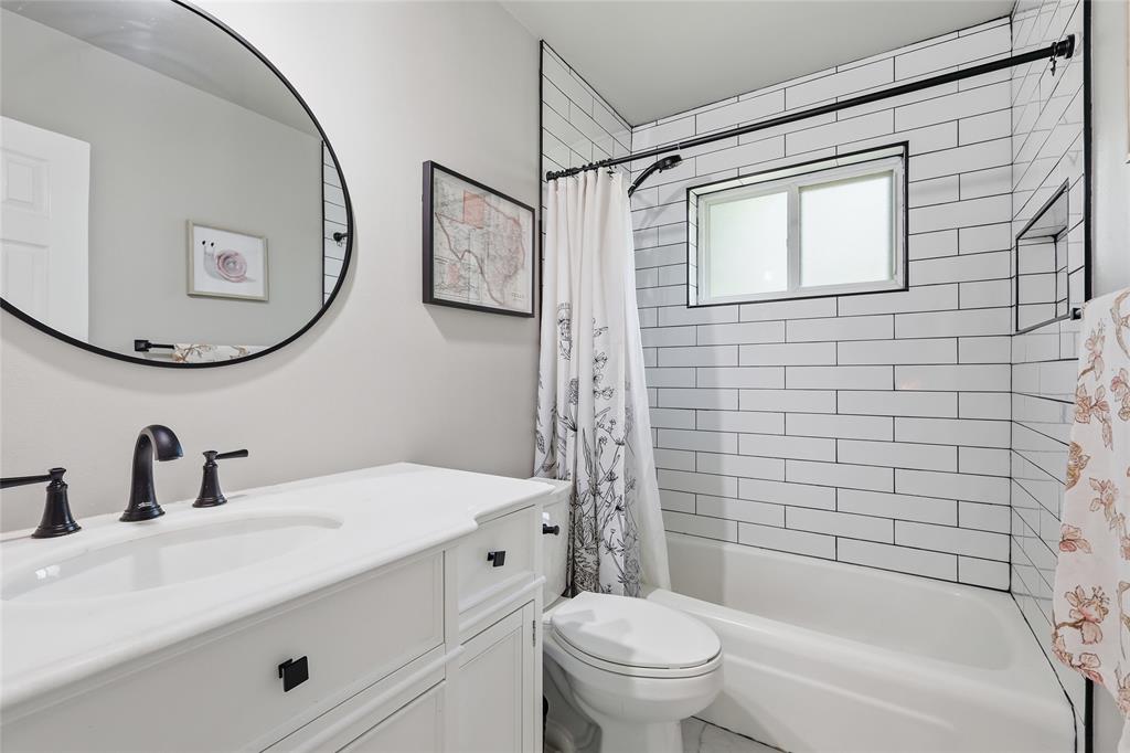 16 Coffee Tavern Road Bedford, TX 76022 - Photo 18 of 24 Bathroom featuring a white subway tile shower surround with a built-in niche, white vanity with black hardware, black-finish faucet, and a round black-frame mirror
