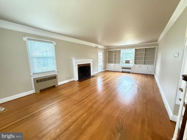 an empty room with wooden floor fireplace and windows