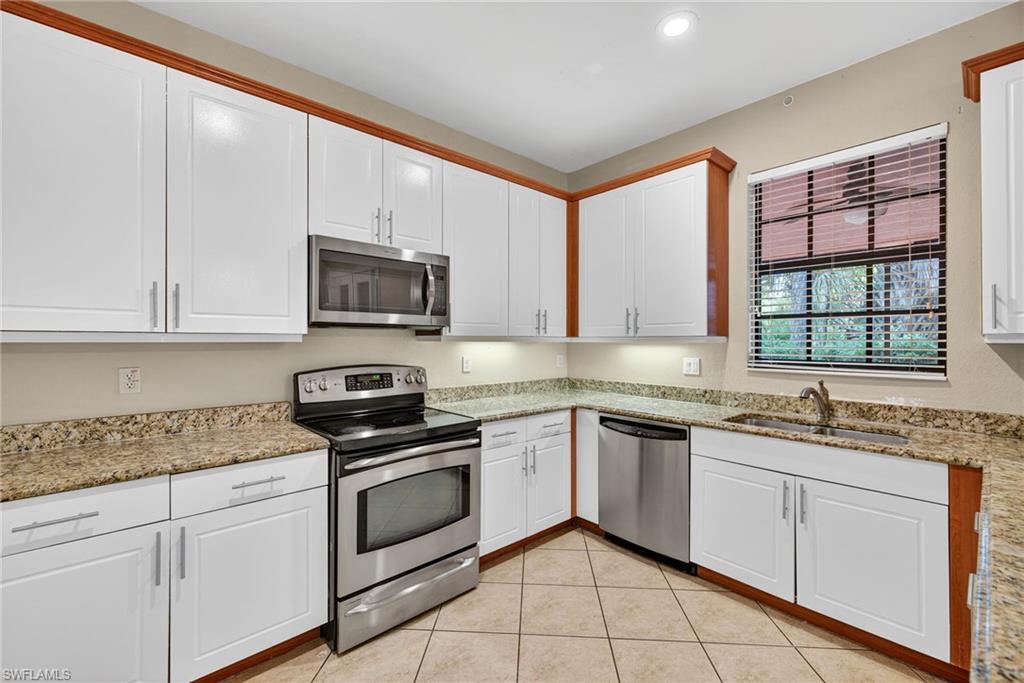 Kitchen featuring stainless steel appliances, white cabinets, and light stone countertops