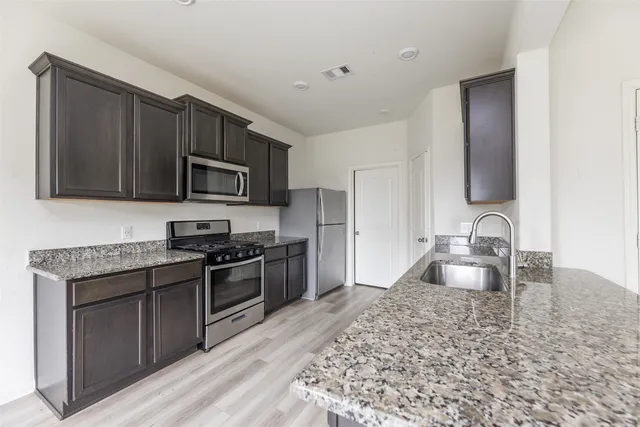 a kitchen with granite countertop a sink wooden cabinets and stainless steel appliances