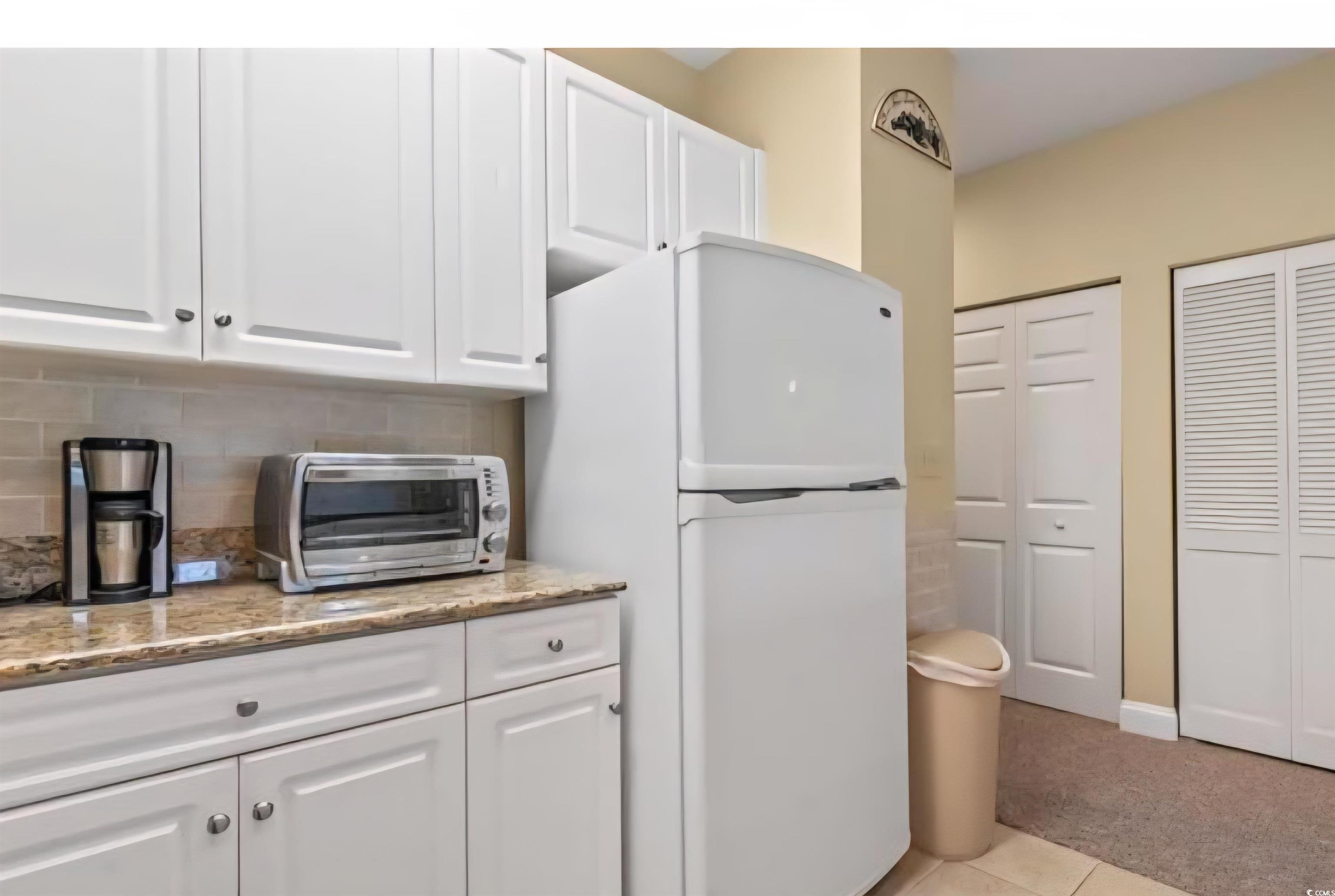 1009 World Tour Boulevard Myrtle Beach, SC 29579 - Photo 32 of 36 Kitchen featuring white cabinetry, freestanding refrigerator, light stone countertops, and tasteful backsplash