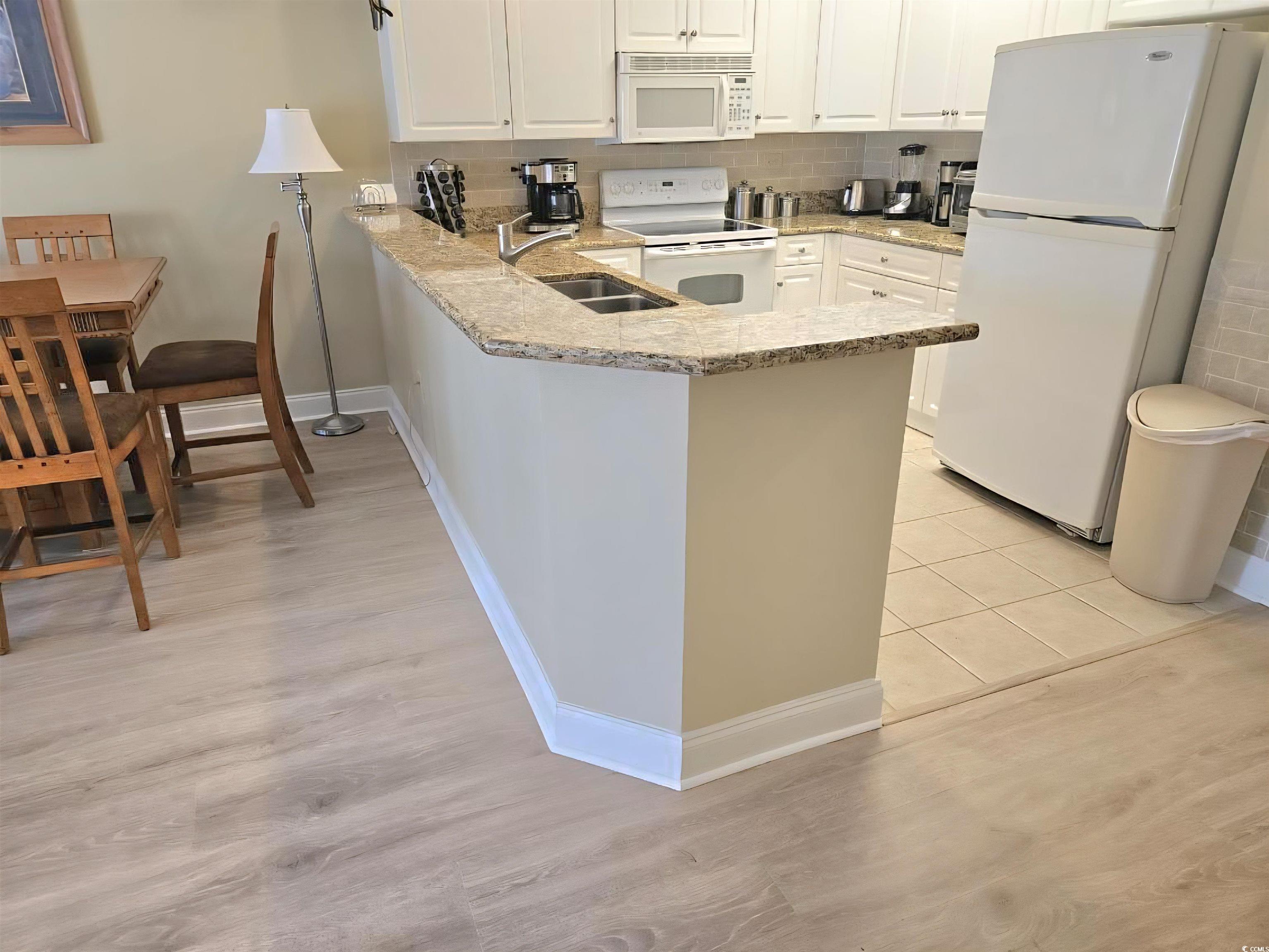 1009 World Tour Boulevard Myrtle Beach, SC 29579 - Photo 4 of 36 new floors . Kitchen featuring tasteful backsplash, white appliances, a peninsula, light stone countertops, and white cabinetry