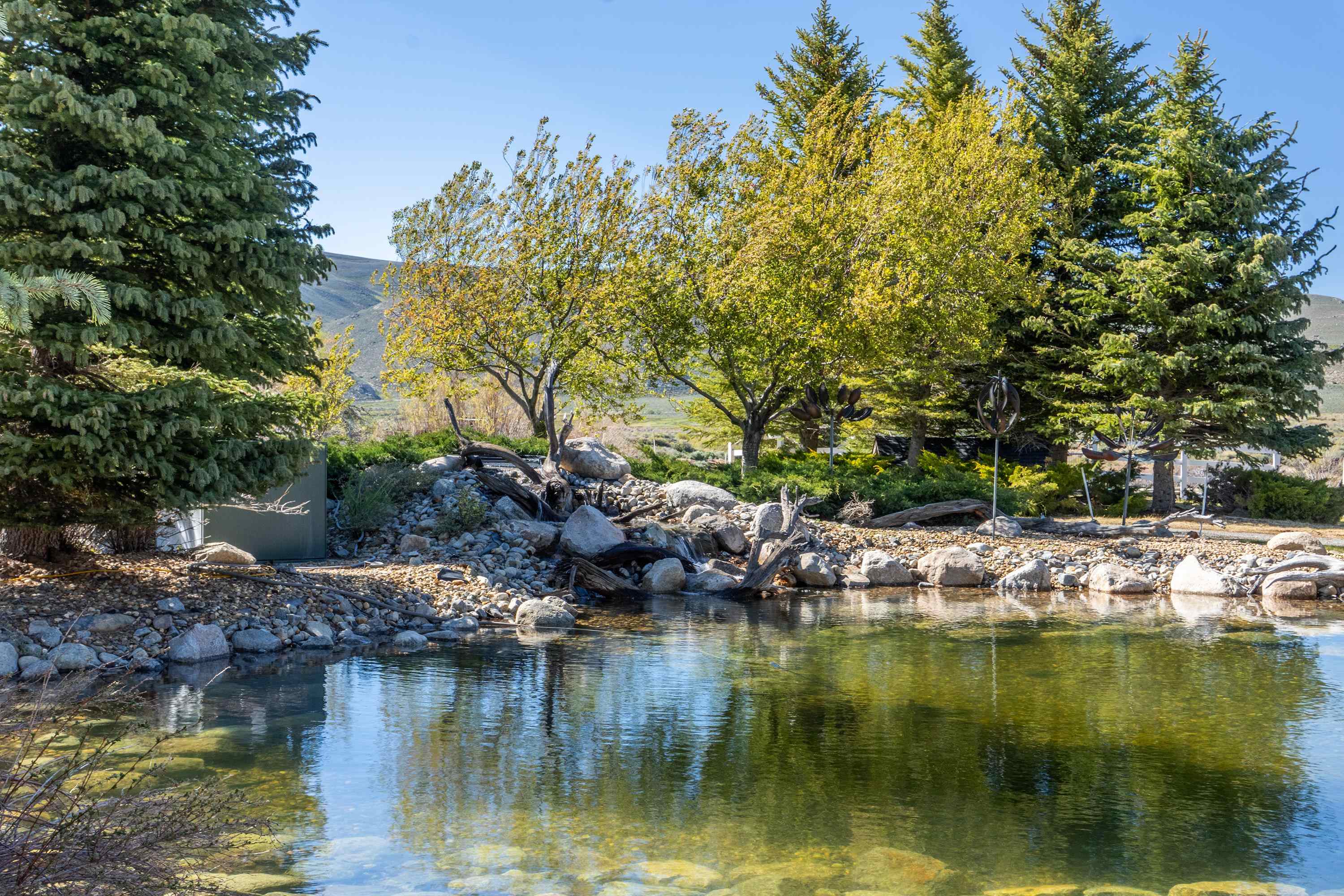 416 Wilson Creek Road Lee Vining, CA 93541 - Photo 53 of 64 Reflective pond with rock-lined edges, surrounded by mature evergreen and deciduous trees
