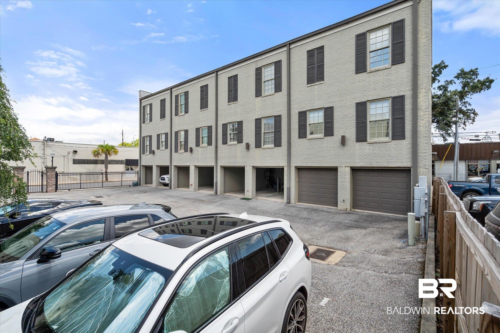 701 Dauphin Street, Unit A Mobile, AL 36602 - Photo 30 of 31 Multi-story brick building with dark window shutters, individual garage doors, and a paved parking area
