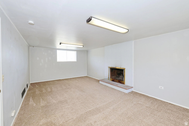 1272 Cook Street Ogden, UT 84404 - Photo 27 of 58 Spacious room featuring neutral carpet flooring, a white painted brick fireplace with a stone hearth, and a window providing natural light