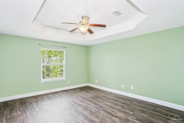 an empty room with wooden floor fan and windows