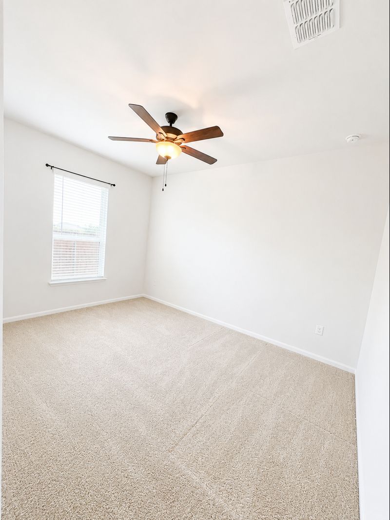 693 Durian Loop Buda, TX 78610 - Photo 4 of 27 A well-lit bedroom with plush carpeting, featuring a window for natural light.