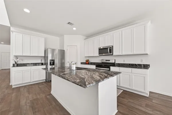 a kitchen with stainless steel appliances granite countertop a stove top oven a refrigerator a sink and dishwasher with wooden floor