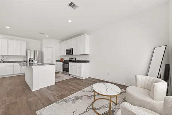 a living room with stainless steel appliances furniture a rug and a kitchen view