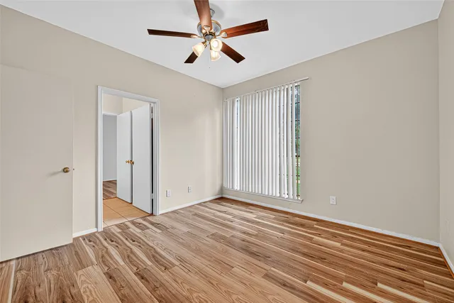an empty room with wooden floor ceiling fan and windows