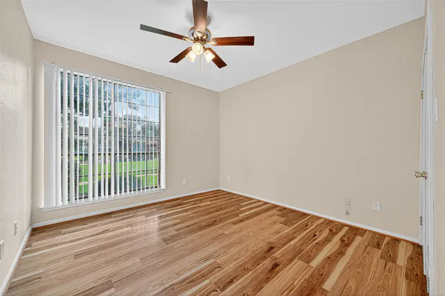 an empty room with wooden floor fan and windows