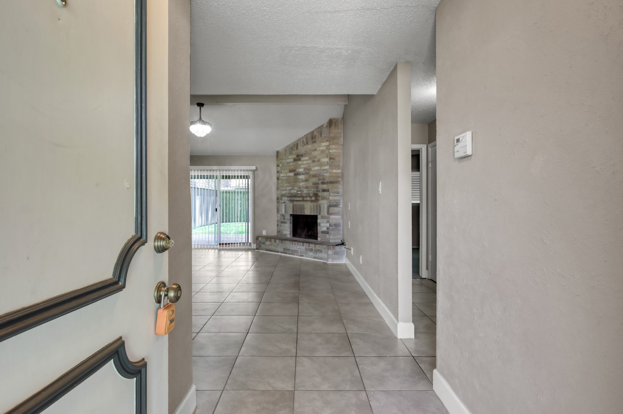 12015 Fallbrook Drive Houston, TX 77065 - Photo 4 of 29 The photo shows the entrance of a home leading to a living area with tiled floors and a stone fireplace. A large window with vertical blinds allows natural light and offers a view of the backyard.