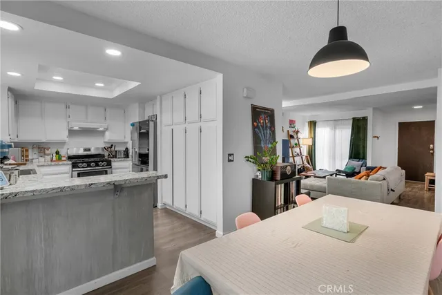 a kitchen with stainless steel appliances kitchen island granite countertop a refrigerator a stove a sink dishwasher and white cabinets with wooden floor