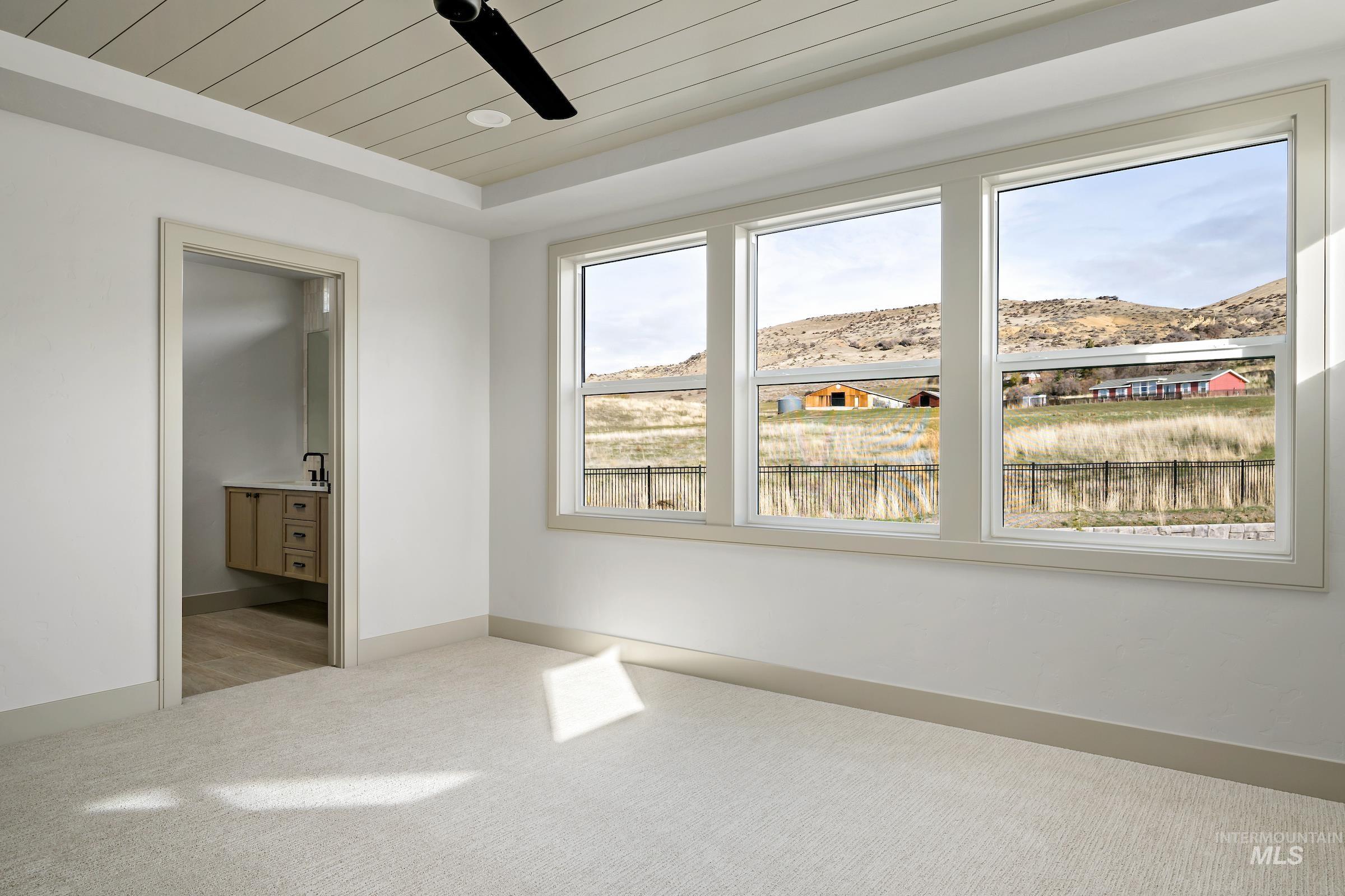 11696 North Rabbitbrush Way Boise, ID 83714 - Photo 23 of 32 Unfurnished bedroom with ensuite bathroom, light colored carpet, wood ceiling, a ceiling fan, and a mountain view