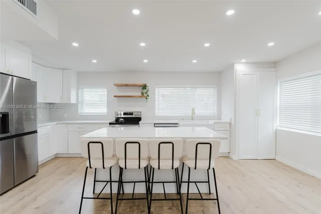 a white kitchen with a stove a sink a refrigerator and white cabinets with wooden floor
