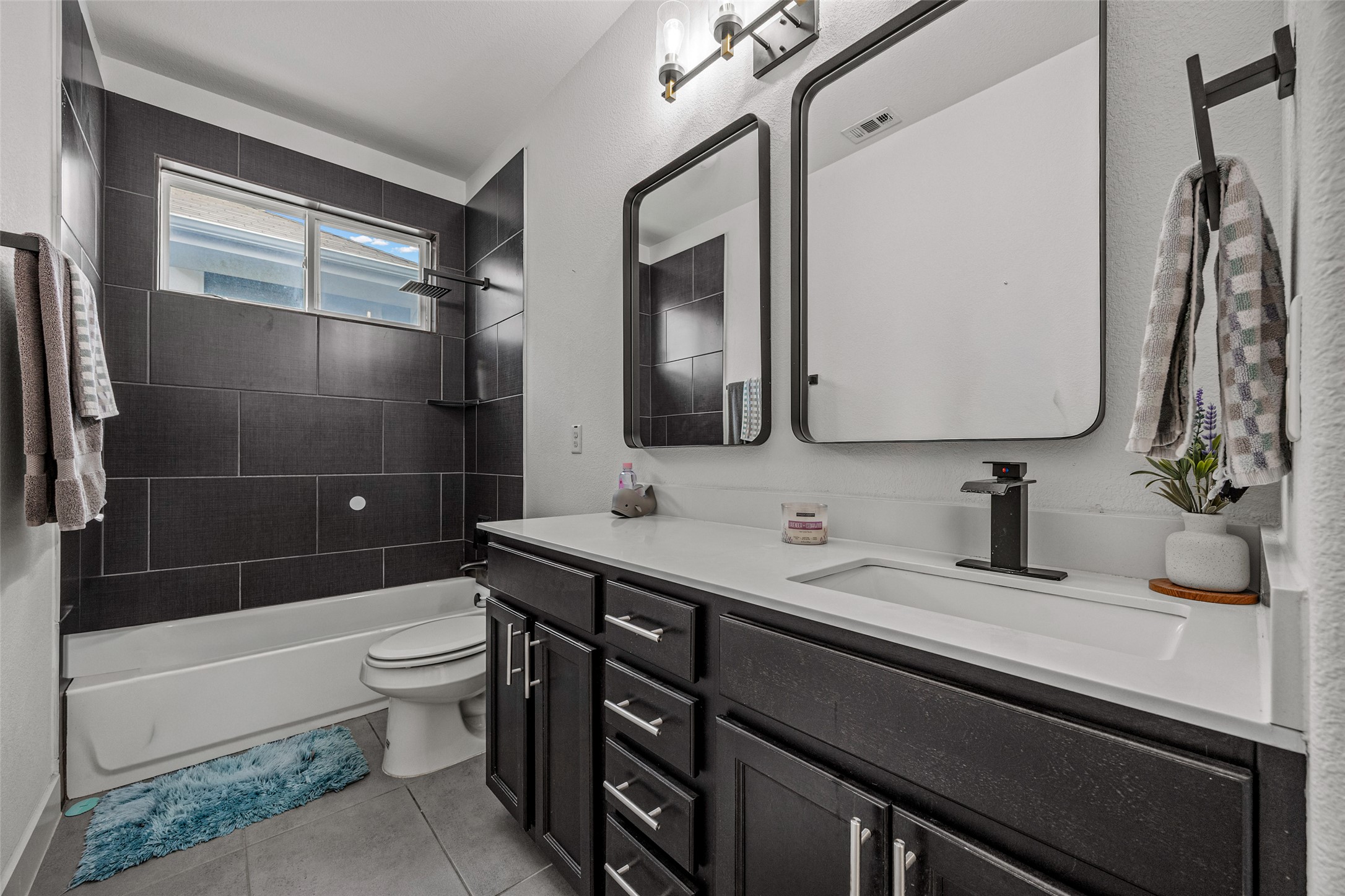 1408 Homespun Road Austin, TX 78745 - Photo 17 of 20 A sleek modern bathroom featuring a deep soaking tub, elegant dark tile, and a spacious vanity with dual mirrors.