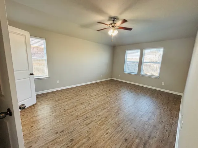 an empty room with wooden floor fan and windows