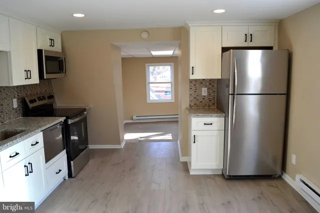 a kitchen with stainless steel appliances a refrigerator a sink a stove and white cabinets with wooden floor