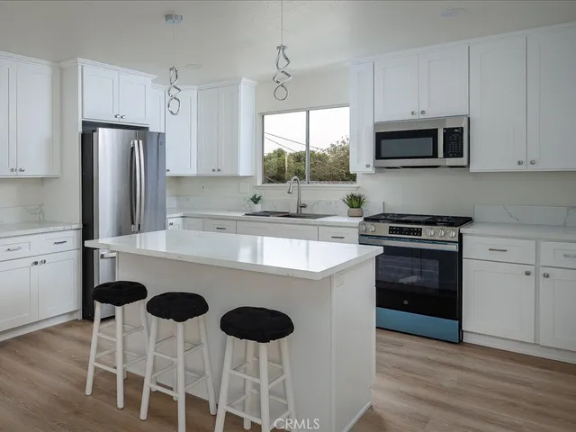 a kitchen with stainless steel appliances granite countertop a stove a sink dishwasher a refrigerator with white cabinets and wooden floor