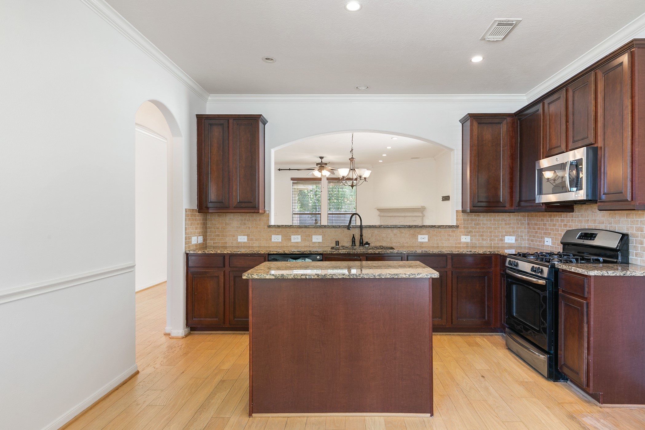 24527 Spring Harbor Drive Spring, TX 77373 - Photo 6 of 22 This is a modern kitchen featuring dark wood cabinetry, granite countertops, and stainless steel appliances, including a gas stove and microwave. An island provides additional prep space, and an arched opening leads to a bright dining area with a chandelier.