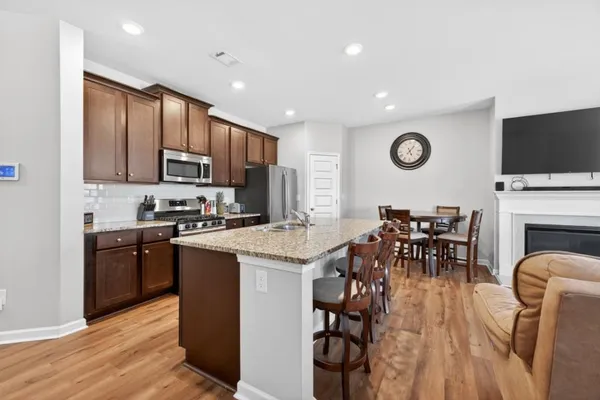 a open kitchen with stainless steel appliances granite countertop a stove top oven a sink dishwasher a dining table and chairs with wooden floor