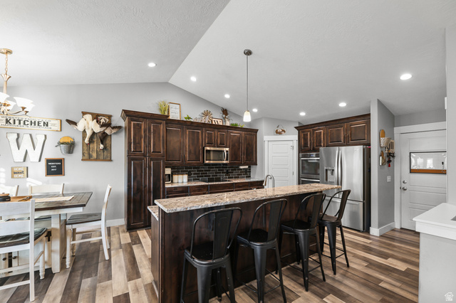 2056 West Ridgeline Road Stockton, UT 84071 - Photo 9 of 50 Kitchen featuring dark wood cabinetry, stainless steel appliances, a center island with bar seating, a tile backsplash, and multi-tone wood-finish flooring