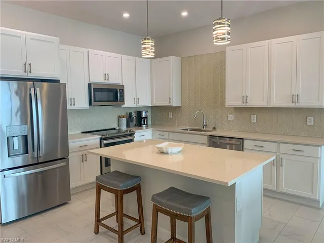 a kitchen with stainless steel appliances a sink a stove a refrigerator cabinets and chairs