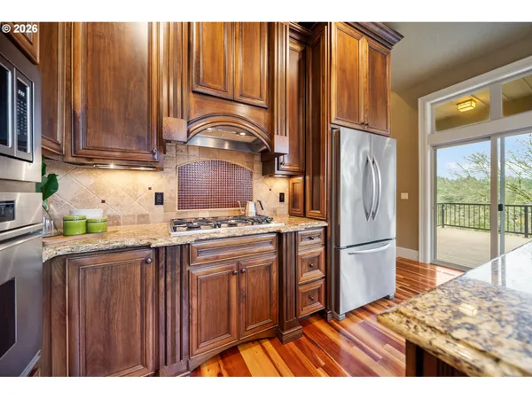 a kitchen with stainless steel appliances granite countertop a refrigerator a stove a sink and dishwasher with wooden cabinets