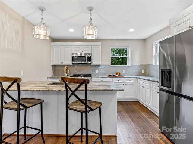 a kitchen with stainless steel appliances granite countertop a stove top oven a refrigerator a sink and a chandelier
