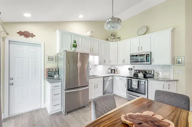 a kitchen with stainless steel appliances granite countertop a refrigerator a sink dishwasher a stove and white cabinets with wooden floor