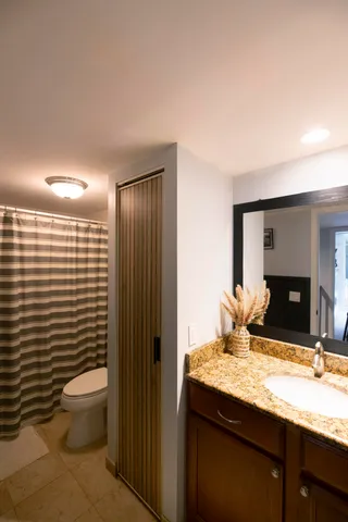 a bathroom with a granite countertop sink a toilet a mirror and shower curtain