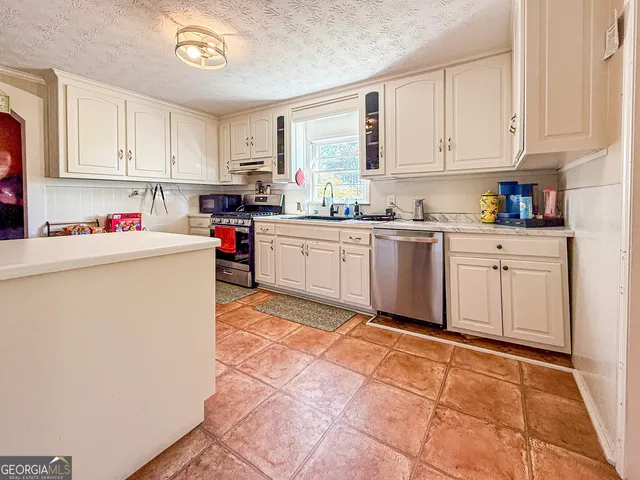 a kitchen with stainless steel appliances granite countertop a stove top oven a sink a refrigerator and white cabinets