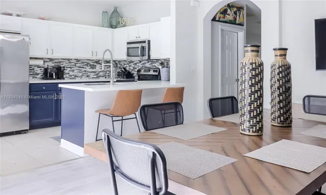 a kitchen with stainless steel appliances kitchen island granite countertop a dining table chairs and a refrigerator