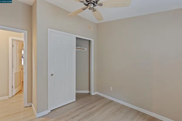 an empty room with a chandelier fan and wooden floor